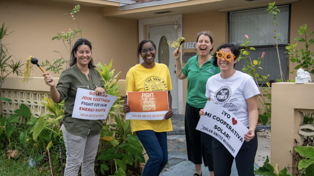 People standing in front of a solar-powered house smiling and holding Go Solar signs